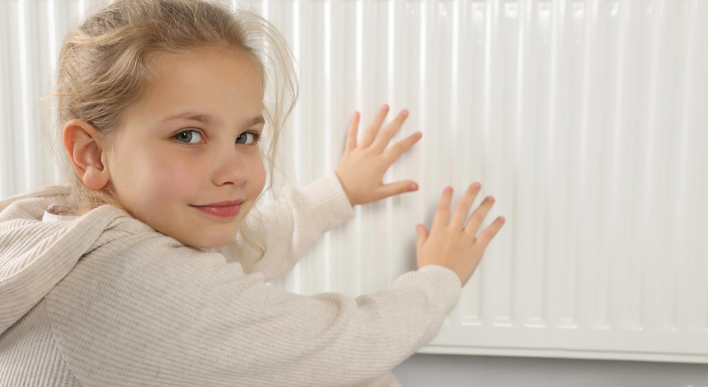 Little girl warming hands near heating radiator indoors