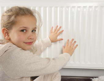 Little girl warming hands near heating radiator indoors