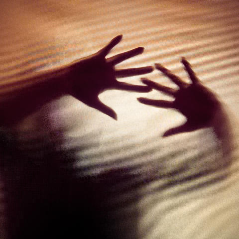 Spooky silhouette of woman with hands pressed against glass window