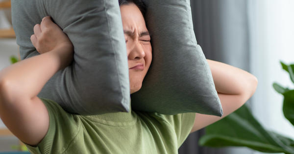 Asian woman having a problems with noise covering ears with pillows sitting at home