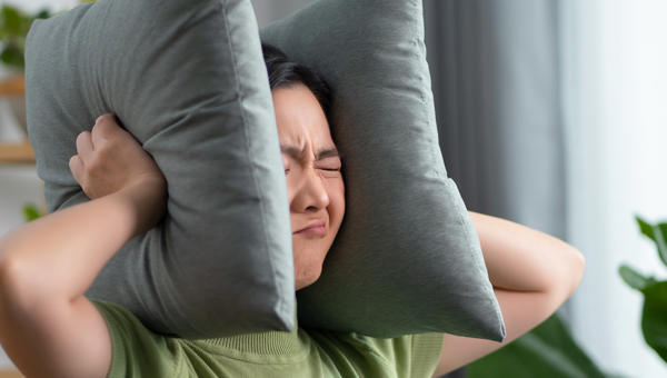 Asian woman having a problems with noise covering ears with pillows sitting at home Asian woman having a problems with noise covering ears with pillows sitting at home