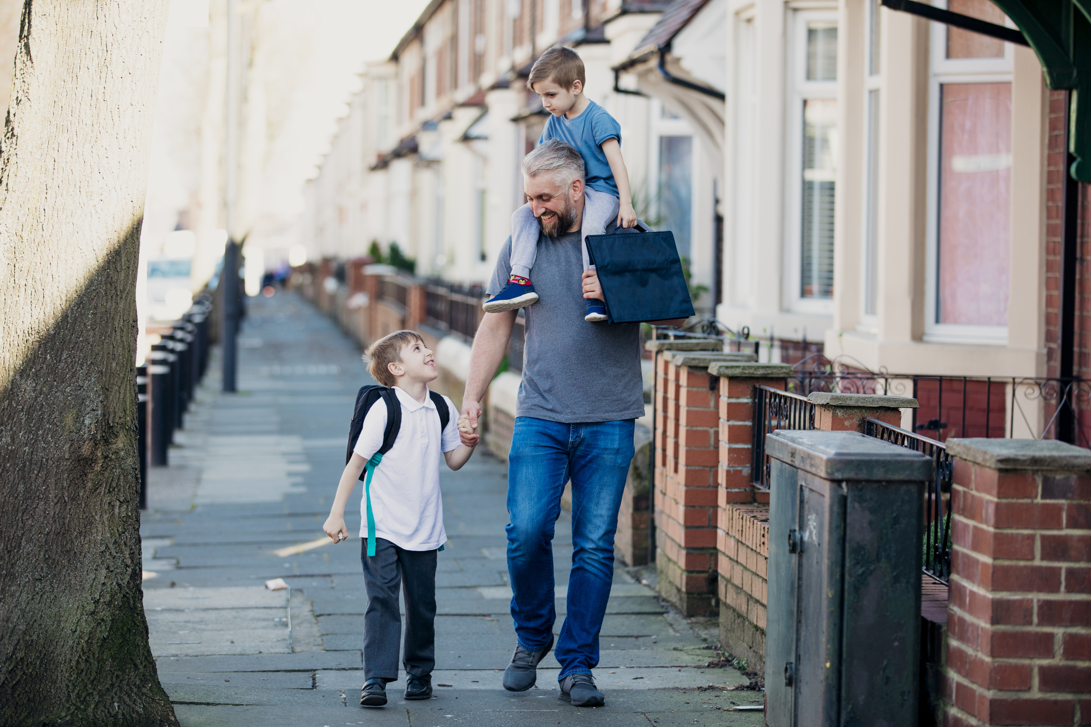 Man walking down residential street with his two young children talking them to school