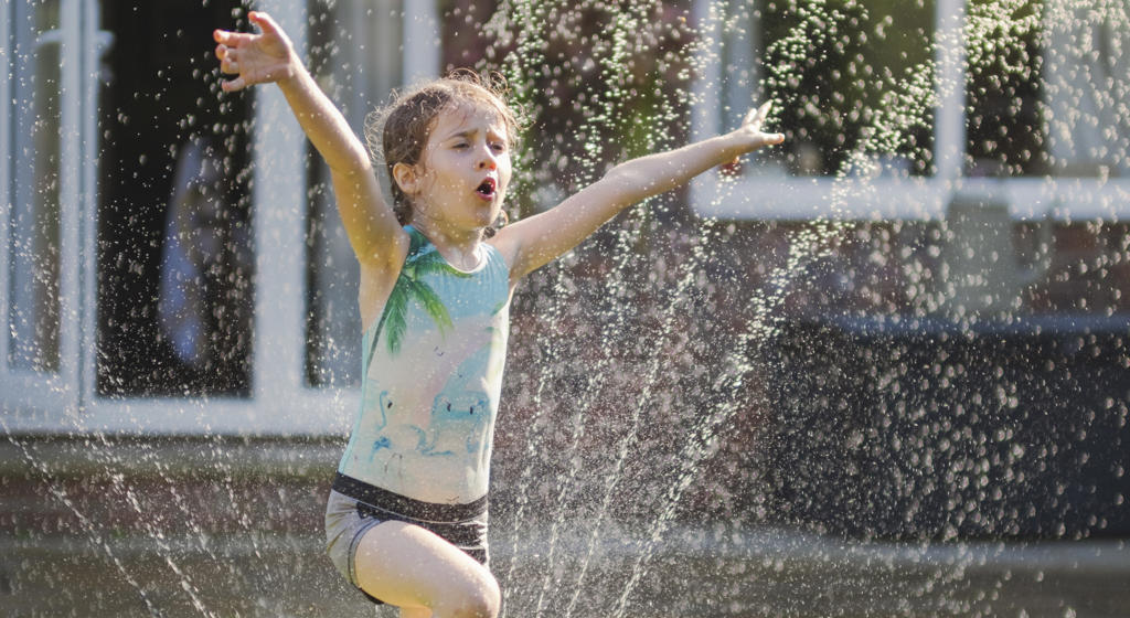 Girl playing in a sprinkler in the garden on a hot sunny day