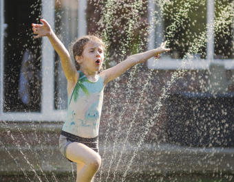 Girl playing in a sprinkler in the garden on a hot sunny day
