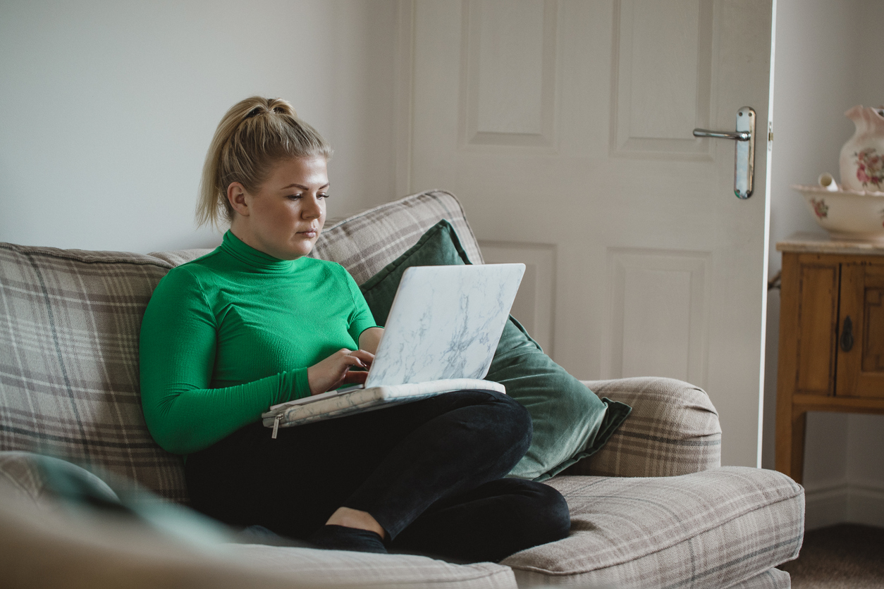 Women in green jumper sat crossed legged on sofa on laptop