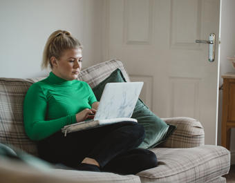 Women in green jumper sat crossed legged on sofa on laptop
