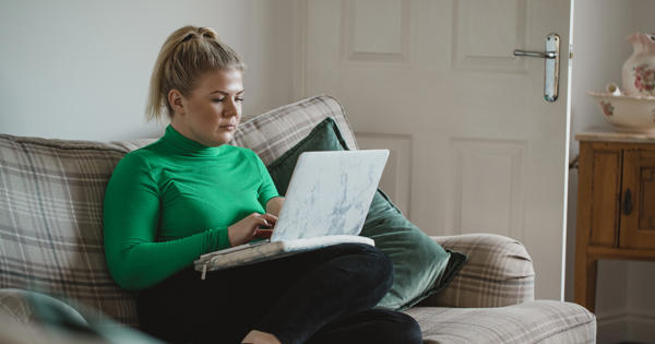 Women in green jumper sat crossed legged on sofa on laptop