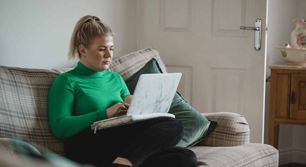 Women in green jumper sat crossed legged on sofa on laptop