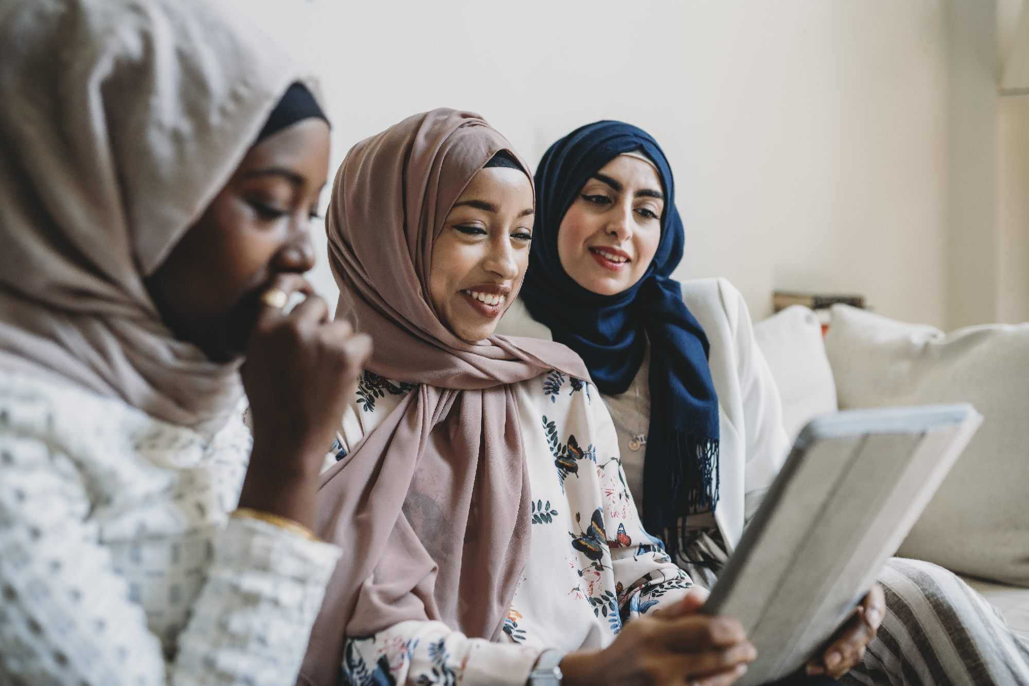 Three Muslim women smiling and using an ipad