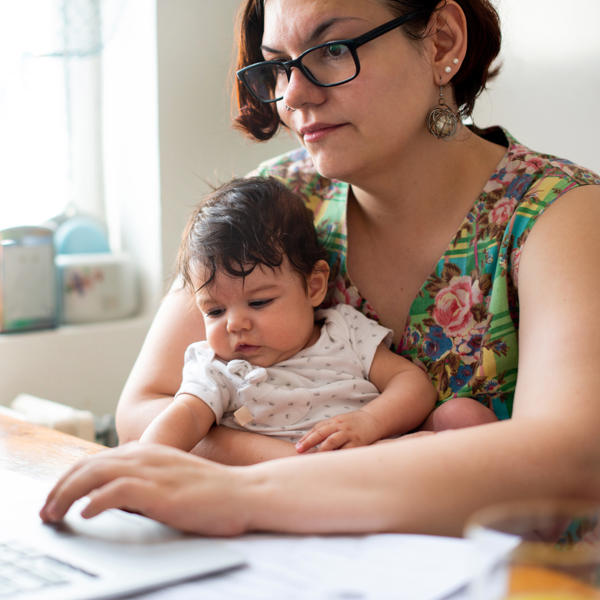 Mother using laptop at kitchen table while holding a young child