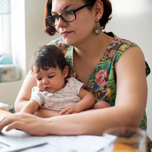 Mother using laptop at kitchen table while holding a young child