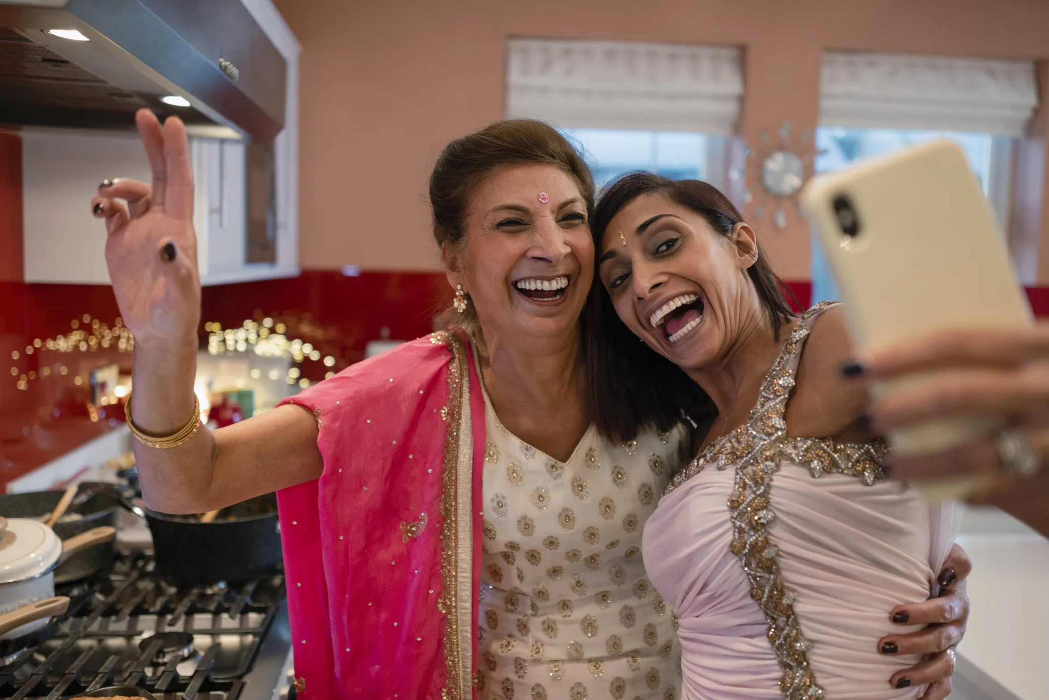 Two Asian women taking a selfie while cooking. Both women are wearing saris.
