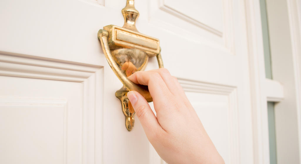 Close up of hand using a brass door knocker on front door