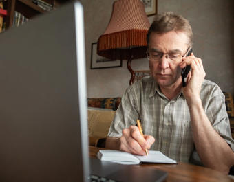 Senior man talking by smartphone and writing down important information