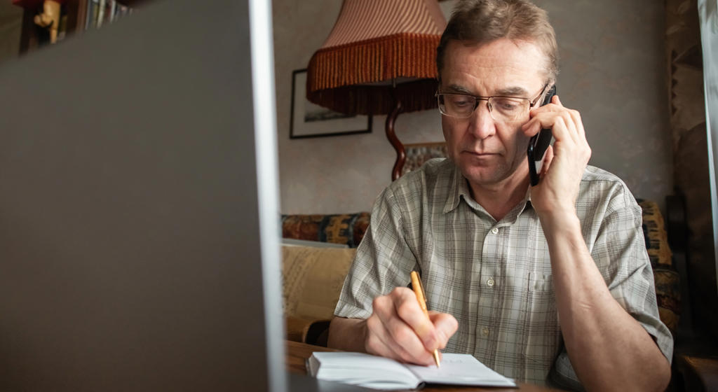 Senior man talking by smartphone and writing down important information