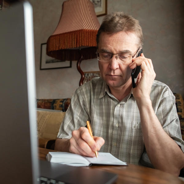 Senior man talking by smartphone and writing down important information