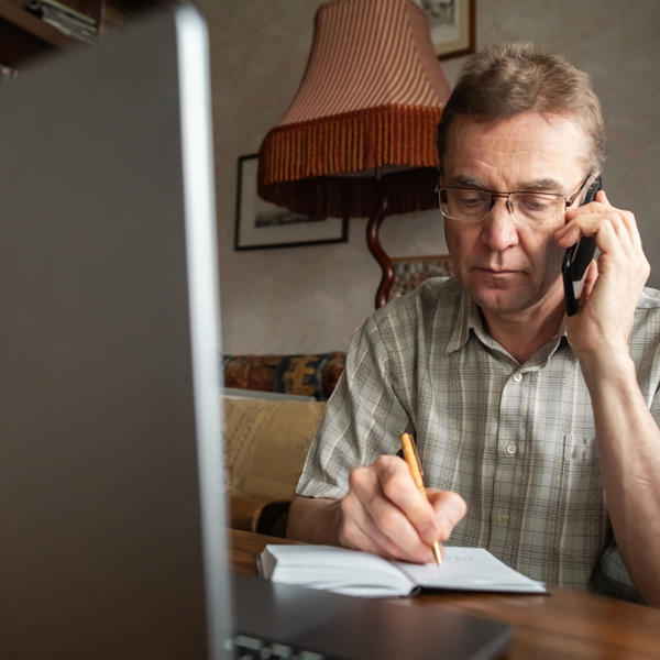 Senior man talking by smartphone and writing down important information