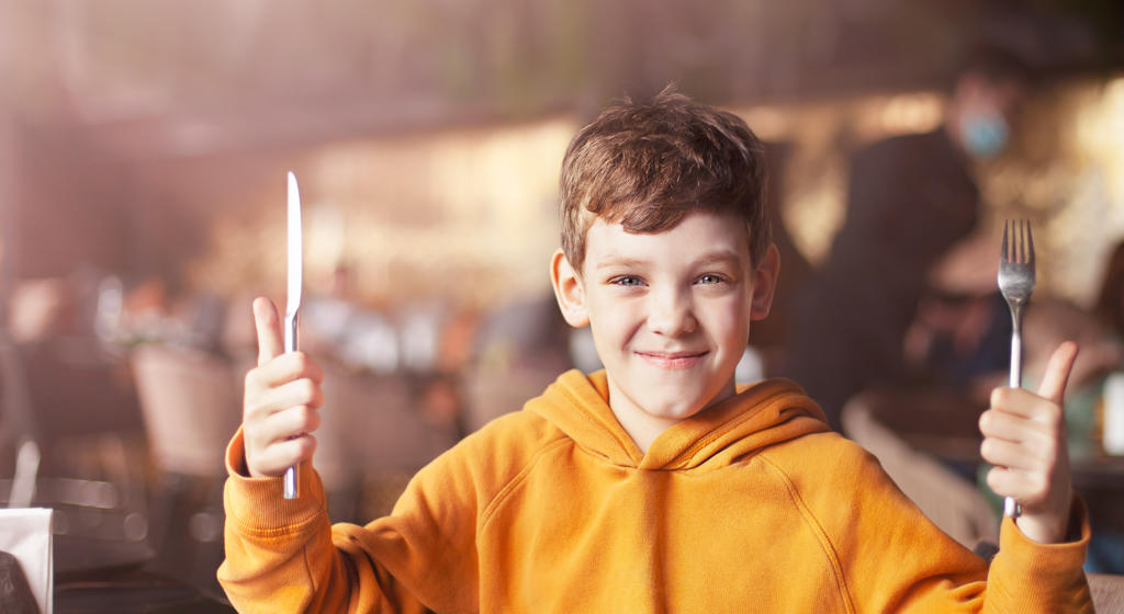 Boy with cutlery in his hands is ready to eat