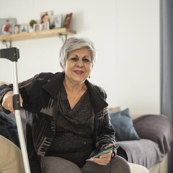 Senior woman lifestyles at home on crutches due to rheumatic disease, smiling at camera