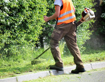 Workman using a strimmer to cut the grass