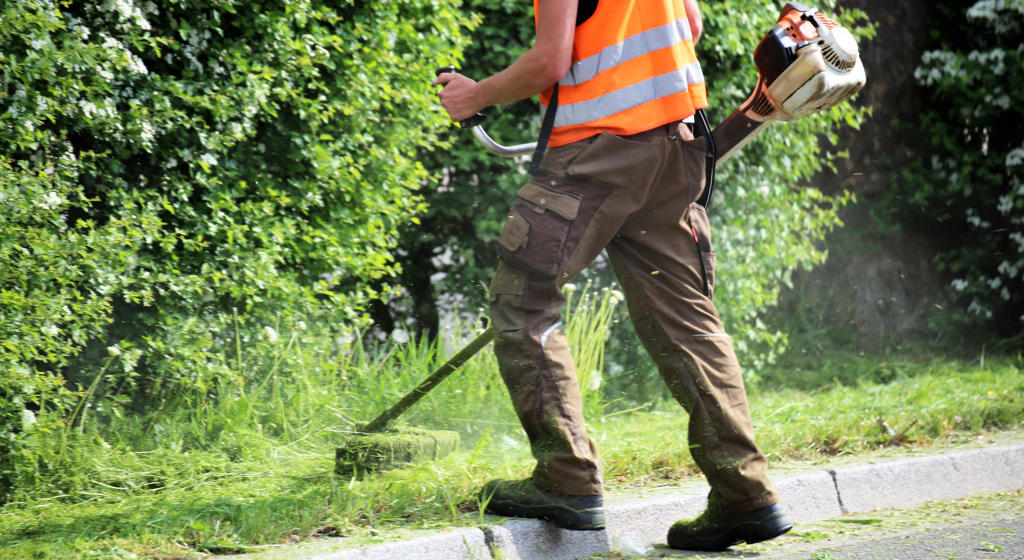 Workman using a strimmer to cut the grass