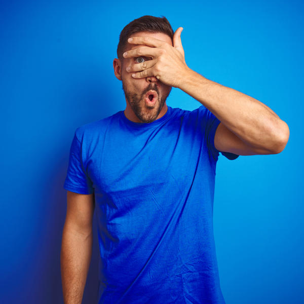 Man t-shirt shocked man, with hand, looking through fingers with embarrassed expression