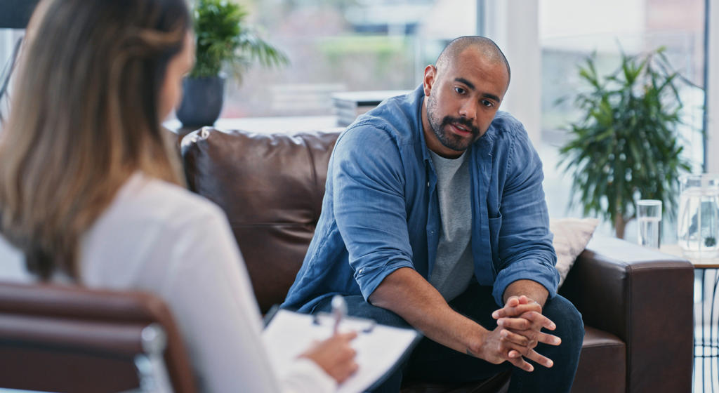 Young man looking thoughtful while sitting in session with his female therapist