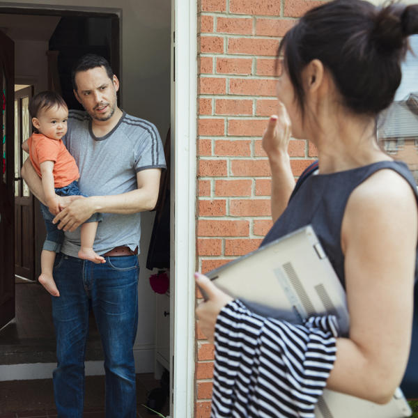 A man stands in the doorway, holding young son while women chats to him from the driveway