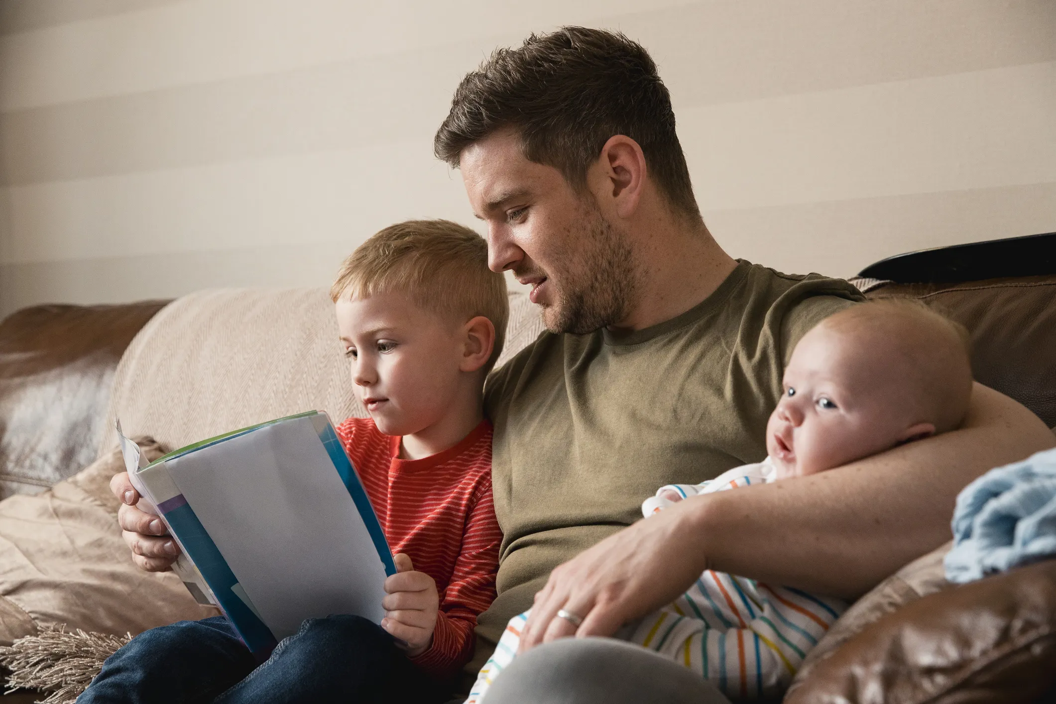 Man with two children sitting on sofa looking at an electronic tablet