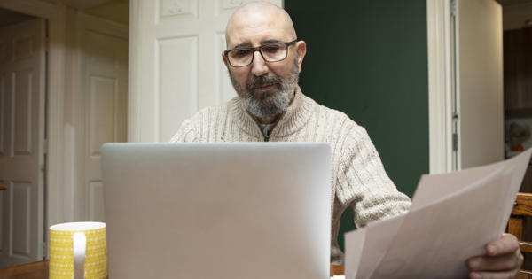 Mature Man Reviewing Financial Information With A Laptop Computer And Paperwork At Home Stock Photo