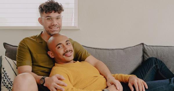 Two men cuddling at home on the sofa looking in love