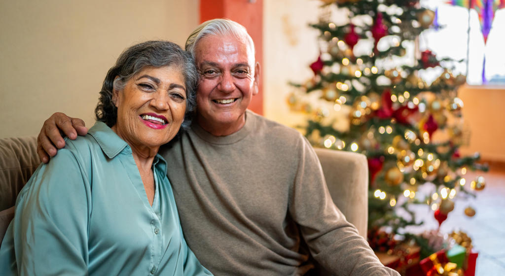Older couple sat on sofa in front of a Christmas Tree