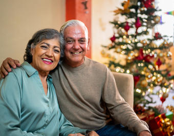 Older couple sat on sofa in front of a Christmas Tree