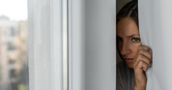 A concerned women peeps through a gap in the curtains