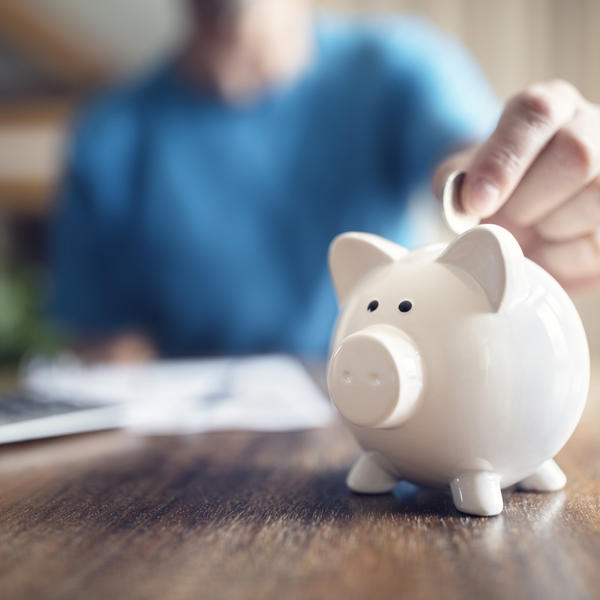 Close up of hand putting coins into a piggy bank