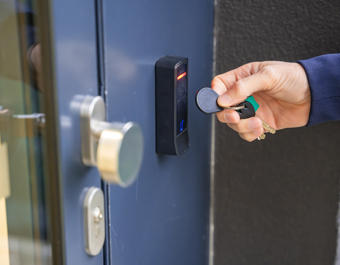 Close Up View Of Person Using A Electric Lock Key Fob To Access A Building Via A Reader Of Entry System Mounted On A House Wall Stock