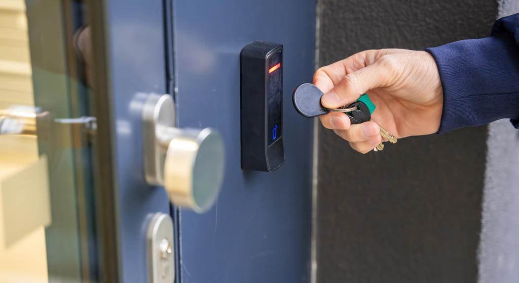Close Up View Of Person Using A Electric Lock Key Fob To Access A Building Via A Reader Of Entry System Mounted On A House Wall Stock