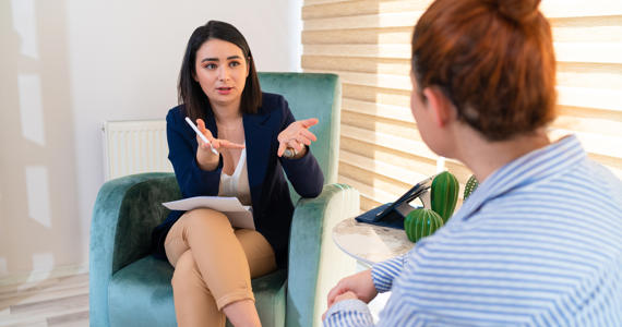 Two white women chatting in the office sat in comfortable chairs